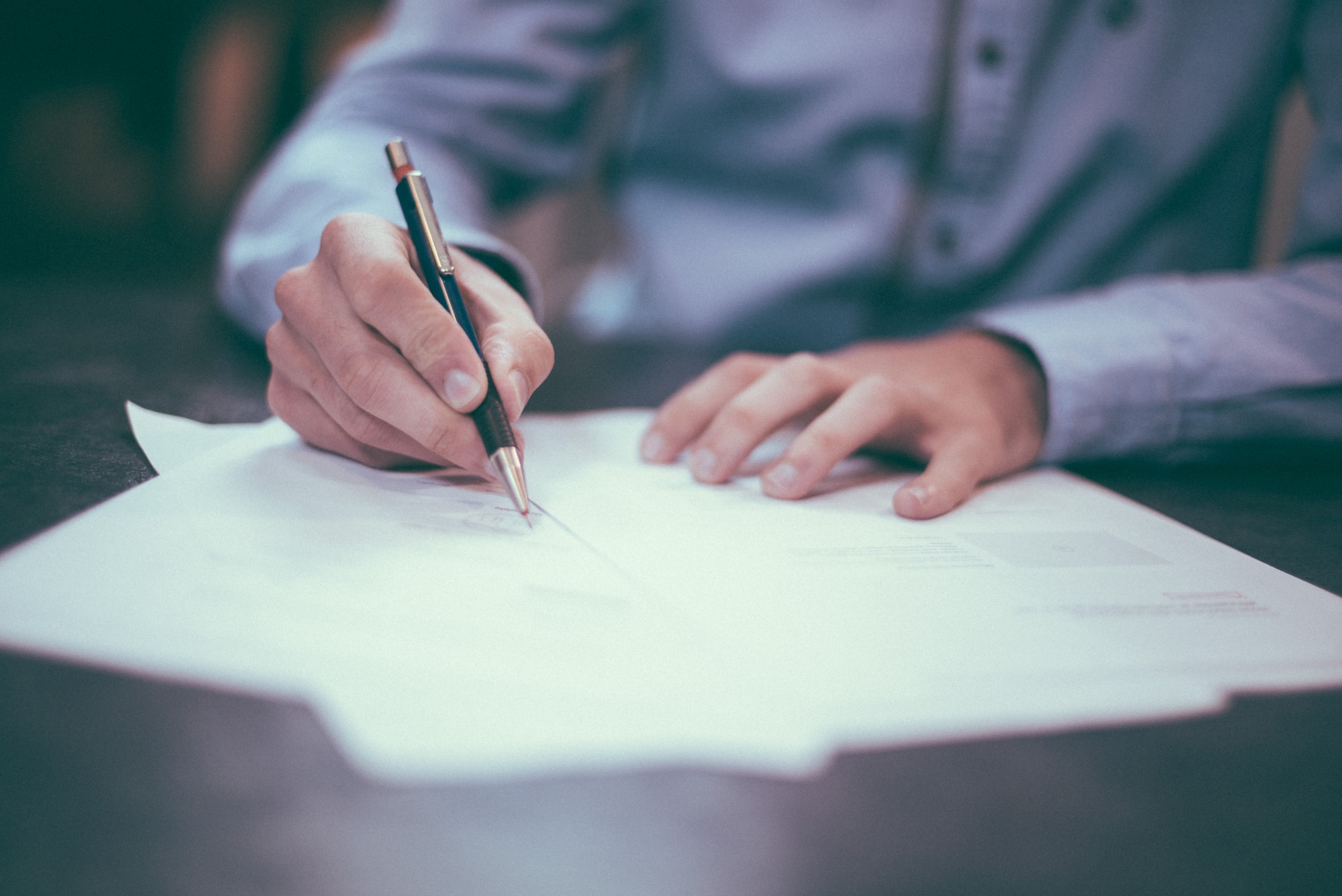 A man wearing a blue shirt writing on papers at a desk