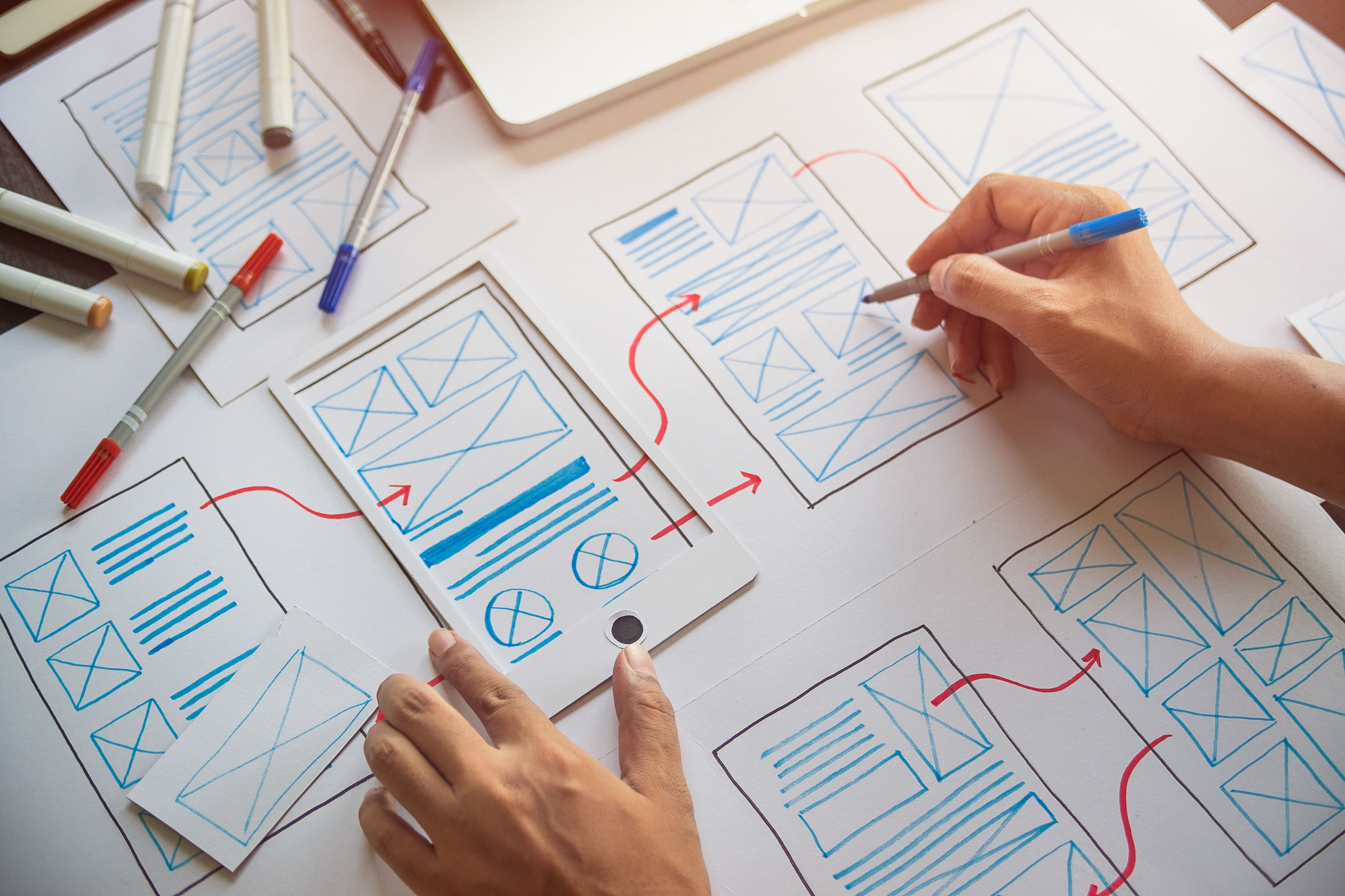 A woman's hand is sketching a series of user interface layouts on a large piece of paper.